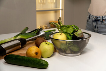 Electric immersion blender with green vegetables and fruits on kitchen