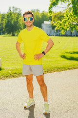 A male athlete in the park, engaging in daily exercise, is smiling and posing while standing on a treadmill.