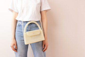 Woman with a handmade bag made from pearl imitation beads over her shoulder in front of beige background. Fashionable accessory.