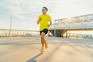 Fototapeta premium Motivation Warm-up a male runner in bright clothes, a T-shirt and sneakers trains during the day.