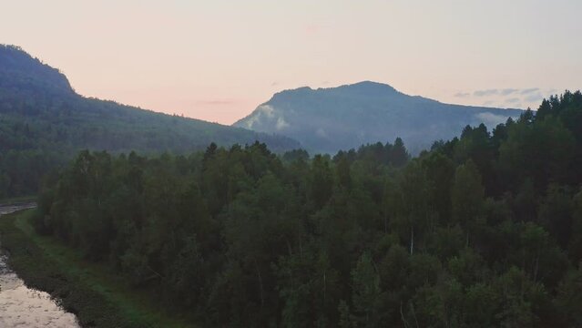 Flying over green tree tops on a sunrise. Morning haze over mountain river