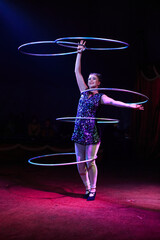 Young slim attractive circus gymnast woman performing live show with hula hoops on red arena with...