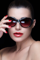 Stylish woman with black oversized sunglasses and red lips posing confidently on a black background