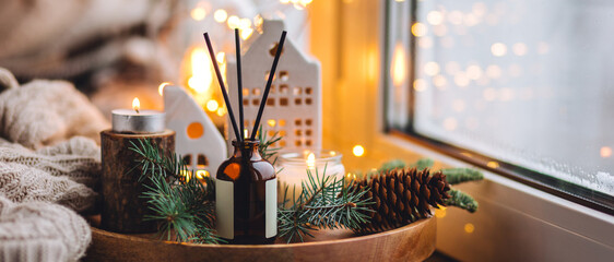 Aroma burning candles, aromatic reed diffuser in glass bottle. Cozy Christmas atmosphere at home. Holiday scent, aromatherapy. Fir tree fragrance, winter mood, decoration, knitted sweater. Banner