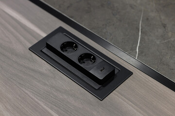 Black built-in electric socket with usb ports on wooden table. A group of European electrical...