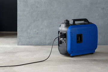 Connected generator. A modern blue portable gasoline inverter generator stands in a garage against a grey wall. Backup autonomous power supply at home. Electricity production and generation.
