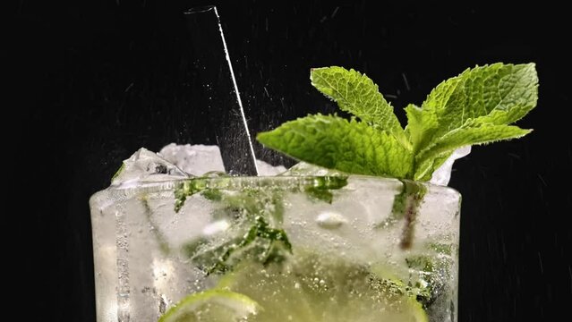 Process of making mojito cocktail. Closeup of pouring sparkling water into glass with ice cubes. Fizzing mojito with ice in glass. Refreshing tasty lime and mint drink.