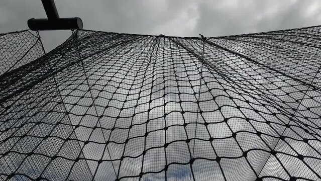 Sports Nets Against a Cloudy Overcast Sky. Looking up a sports netting used to enclose a batting cage. The nets move with the wind in slow motion.  