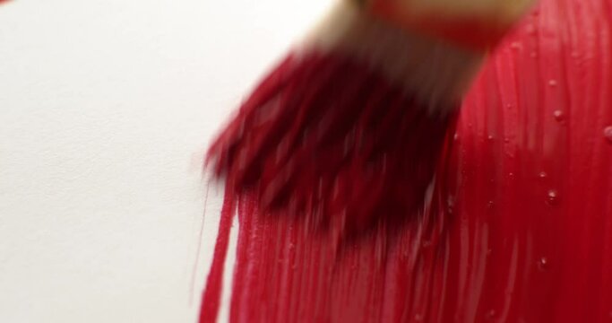 Close up of an artist's paintbrush with brush strokes painting vibrant red paint covering the canvas creating a solid red background.
