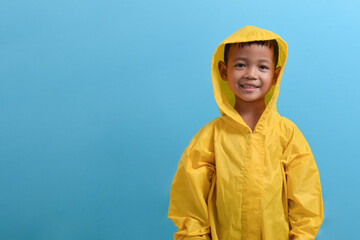 Cute little Asian boy wearing a yellow raincoat isolated on blue background. Weather forecast...