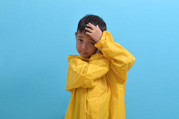 Cute little Asian boy wearing a yellow raincoat isolated on blue background. Weather forecast concept
