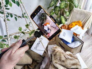 The blogger takes off stacks of clothes and signs with the words save, donate, throw away on cell phone. The concept of clutter, a debacle for a blog