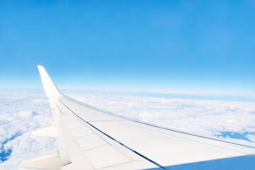 Obraz premium White wing of the airplane against the blue sky and white clouds skyline View from aircraft window