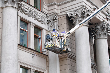 Utility workers on lift platform, facade restoration on historic building with ornate columns,...