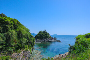 A rope fence leads to a small sandy island with a few rocks in the foreground all surrounded by a bright blue ocean.