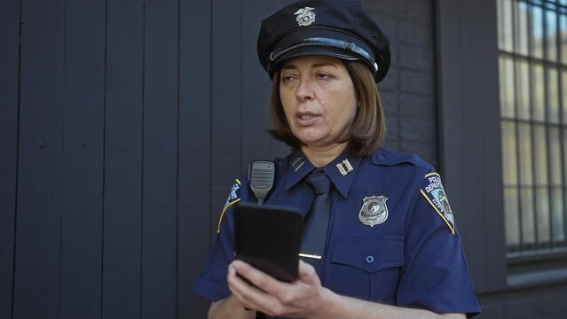 Mature hispanic policewoman in uniform using notepad outdoors in an urban environment