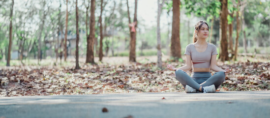 A woman is sitting on the ground in a park, looking up at the sky. She is wearing a grey shirt and...