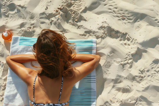 Woman sunbathing on the sand on the beach on her vacation trip, with her back tanning under the sun, indulging in the calm and beauty of her seaside trip