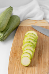 Close Up of One Zucchini Sliced on a Cutting Board with Whole Zucchini in the Background