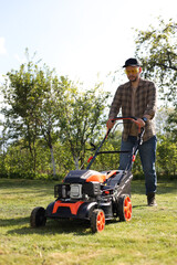 Fototapeta premium Man cutting green grass with lawn mower in garden