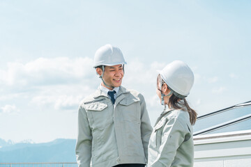 太陽光発電・ソーラーパネルの前に立つ電力会社・電気工事業者の作業着姿の技術者・ビジネスパーソン
