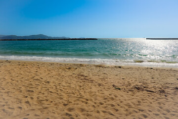 Fototapeta premium a deserted sandy beach with calm, blue water and blue sky in the background.
