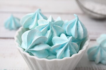 Tasty meringue cookies in bowl on white wooden table, closeup