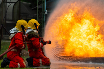 Firefighters teamwork in fire suit on rescue duty using water from hose extinguishing fighting with...