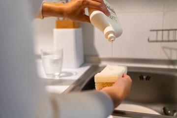 Happy Asian woman do housework washing dishes in the sink after dinner in the kitchen at apartment. Attractive girl using dishwashing liquid and sponge cleaning kitchenware at home kitchen in evening.