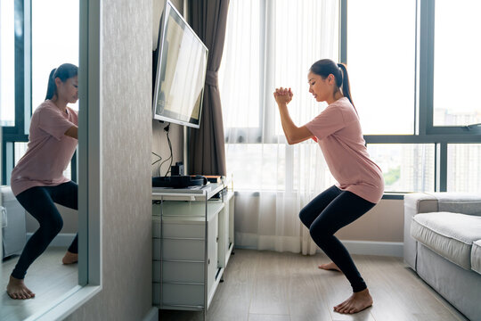 Healthy Asian woman in sportswear do sport workout exercise by watching exercise tutorials online class on smart TV with internet in living room at apartment. Smart home fitness and technology concept