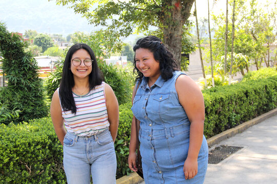 Two young women sisters and brunette latin friends walk and talk in the park spend time together after school
