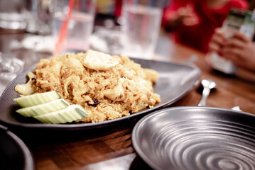 Green chicken curry fried rice dish with blurry customer hands background, nuts, cucumber slices served on wooden bowl at upscale Thai restaurant in Austin, Texas, Asian food lunch dinner dish
