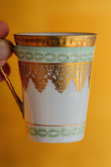 ornate while ceramic Turkish coffee cup with gold and green filigree designs against gold backdrop