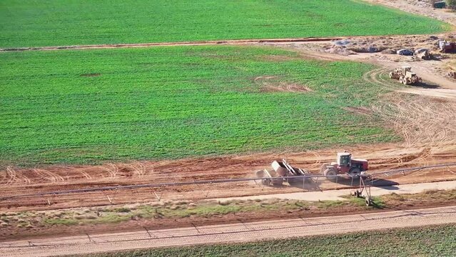 Tractor and small road grader driving on farm dirt road beside other farm equipment