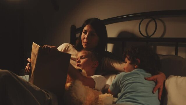 Girl reading bedtime story to her brother with their mother by their side cozy nighttime scene. Family bonding and bedtime routines concept