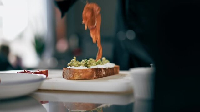 close up in a professional kitchen a chef in a black jacket puts salmon on toast with tweezers
