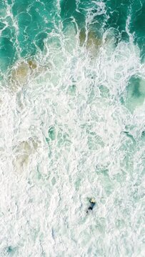 Vertical Screen: Aerial footage showcases a skilled surfer successfully conquering powerful ocean waves. Gripping topview perspective captures the intense and thrilling moment from above