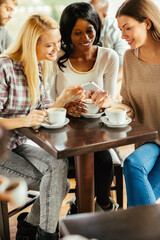 Three women looking at smartphone and enjoying coffee at a cafe table