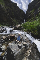 toy teddy bear traveler rests at a waterfall in a mountain river in a gorge in the Aksu-Jabagly Nature Reserve in Kazakhstan in summer