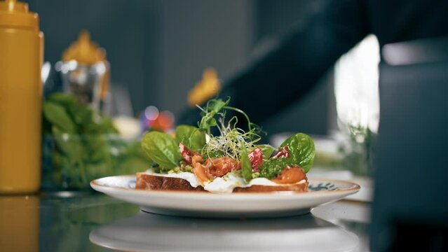 close up in a professional kitchen in a patterned plate there is ready-made toast with salmon and herbs