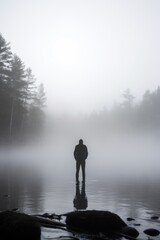 Fototapeta premium A man stands on a lake in the fog. The scene is quiet and peaceful, with the man being the only person in the image. The fog adds a sense of mystery and solitude to the scene