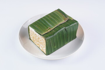 Raw tempeh wrapped in Indonesian banana leaves on a white plate on a white background with studio lighting