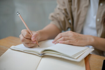 A female college student holding a pencil, writing something in a notebook at a table indoors.