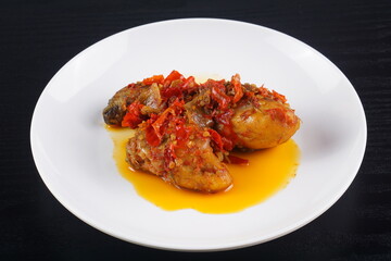 Indonesian typical balado fried chicken on a white plate on a black background with studio lighting