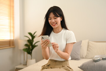 Pretty young woman using mobile phone while sitting on bed at home
