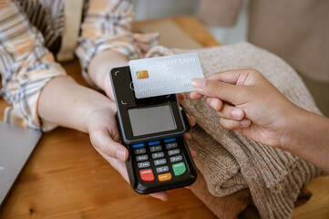 A close-up image of a customer tapping her credit card with a payment terminal in a clothing store.