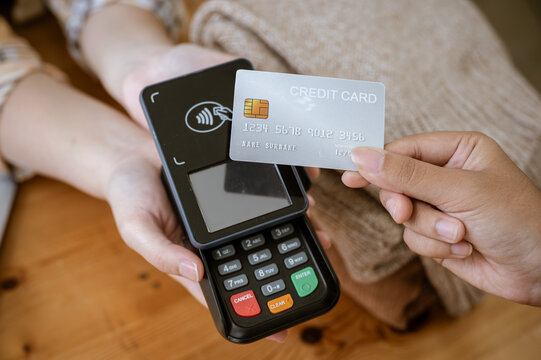 A close-up image of a customer tapping her credit card with a payment terminal in a clothing store.