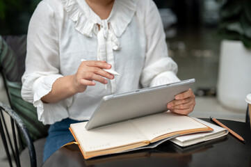 A cropped image of a woman holding a stylus pen, writing or drawing on her digital tablet.