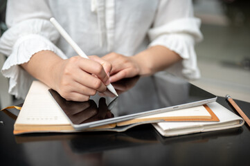 A cropped image of a woman holding a stylus pen, writing or drawing on her digital tablet.
