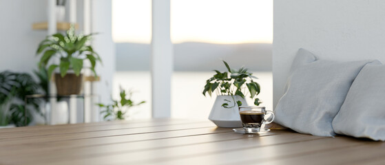 A wooden tabletop featuring a coffee cup, a potted plant, and pillows in a minimalist living room.